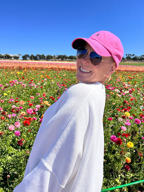 A picture of Club Pilates member Michelle L after being diagnosed as cancer free in a field of flowers, smiling