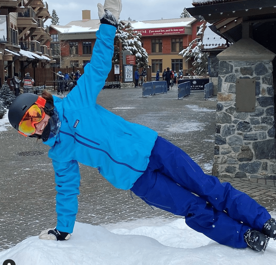 Smiling girl doing side plank in ski gear on mountain